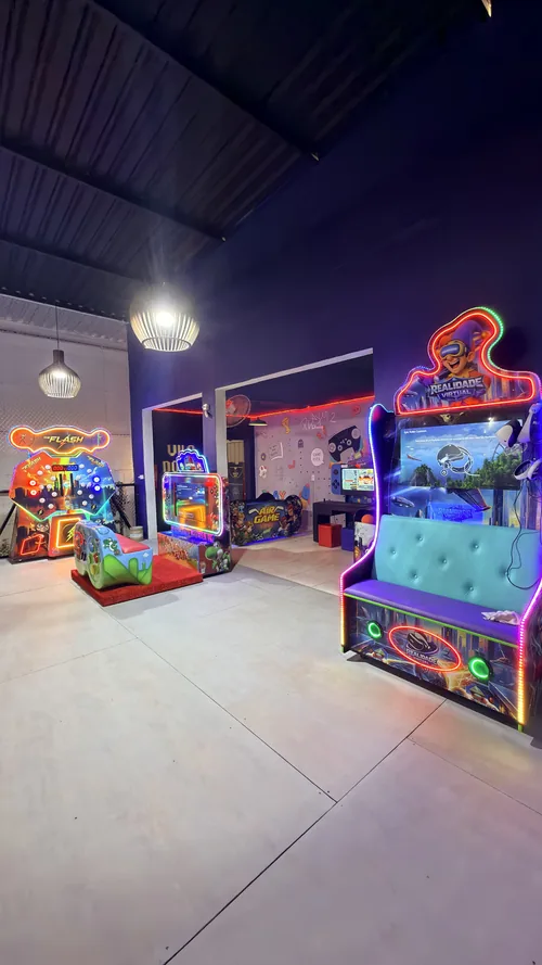 Sala de jogos do Espaço Vila do Sol com fliperamas em neon e cabine de realidade virtual