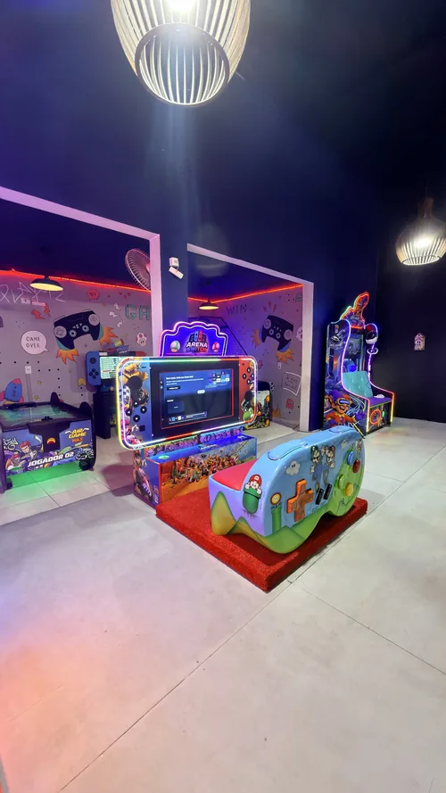Arena de games com telão, poltrona em formato de controle de videogame e fliperama em neon, no Espaço Vila do Sol em Divinópolis